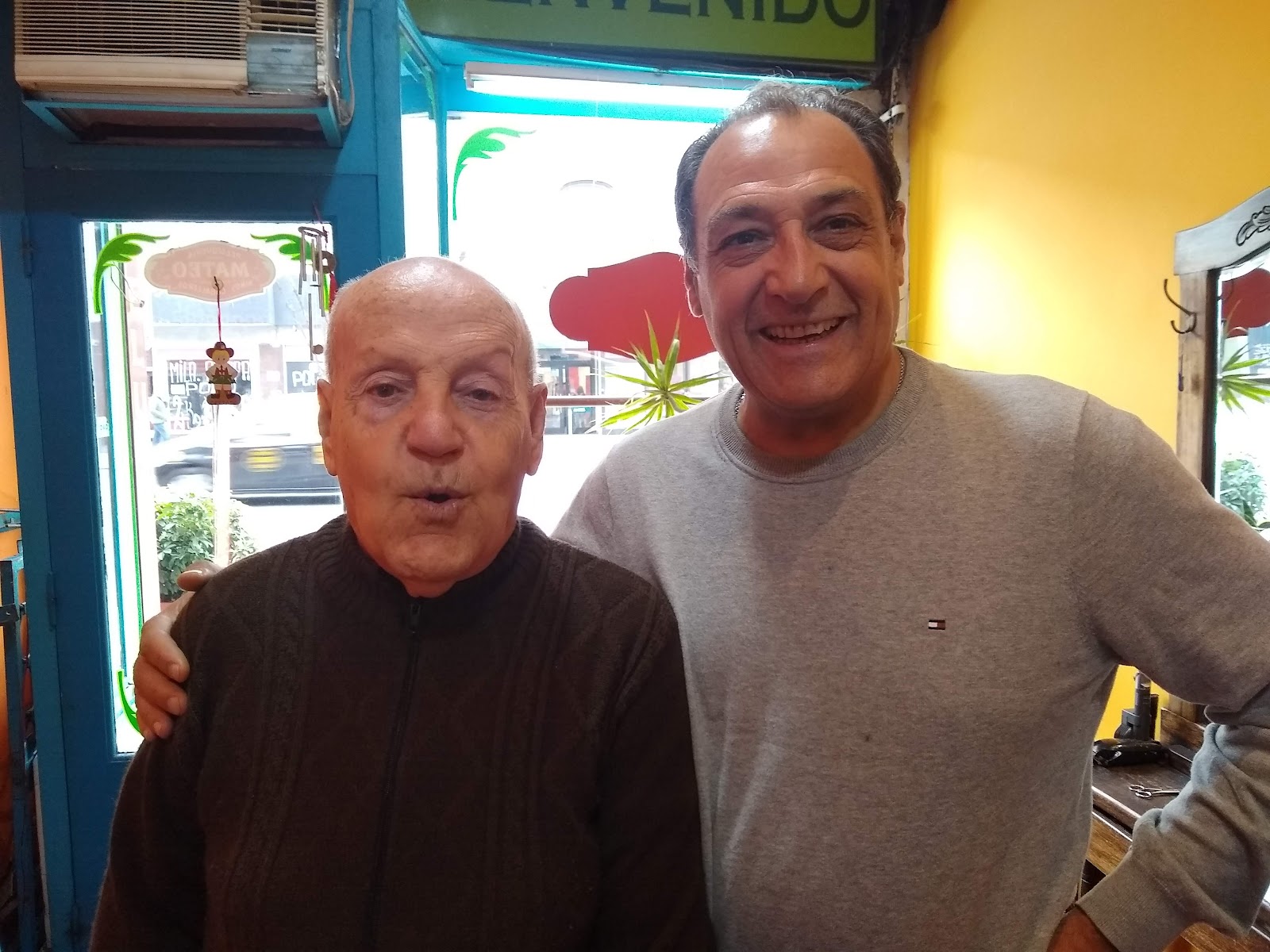 Mateo sonriendo junto a un cliente de años en la puerta de la peluquería