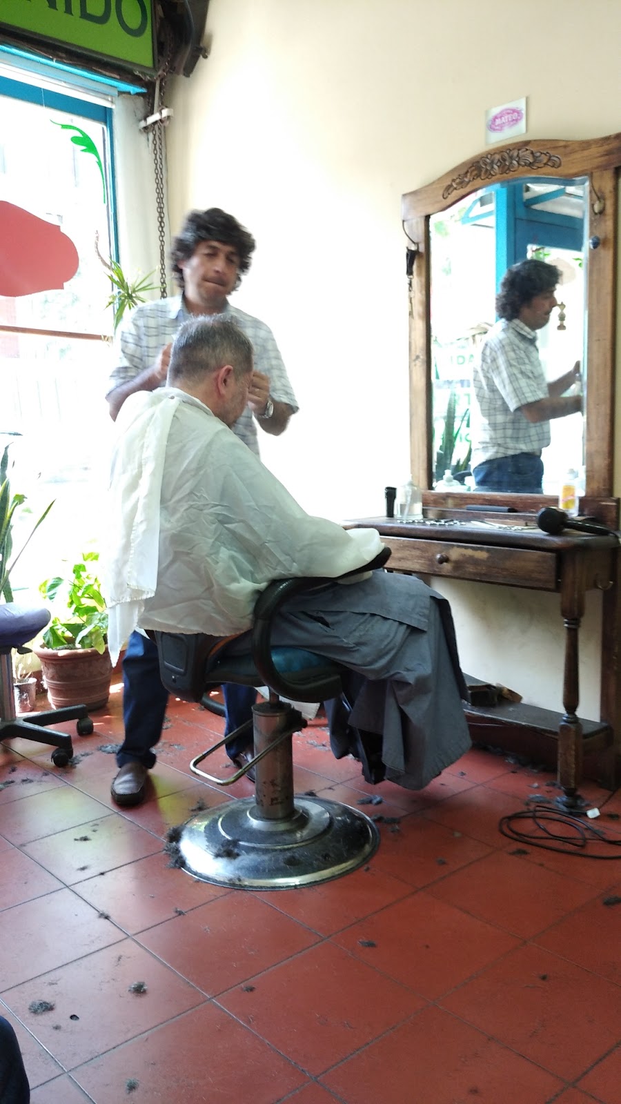 Mateo cortando el pelo a un cliente frente al espejo antiguo de madera
